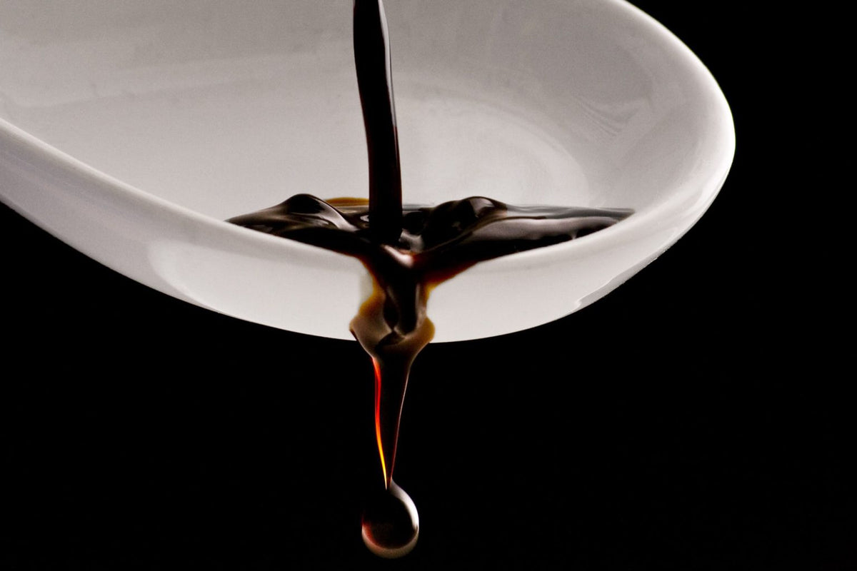 Thick balsamic vinegar pouring into a white spoon against a black background.