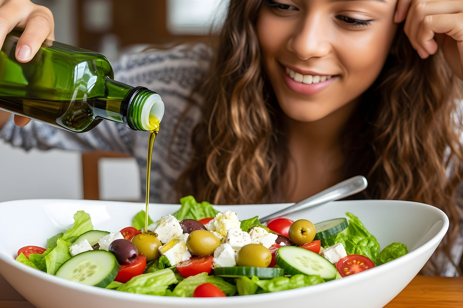 Woman pouring extra virgin olive oil over a salad with lettuce, tomatoes, cucumbers, olives and feta cheese.