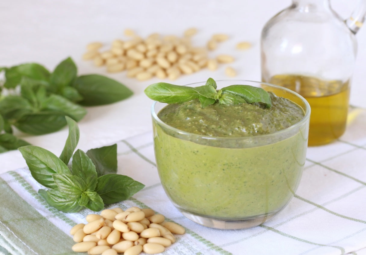 Pesto alla Genovese in a glass bowl with fresh basil leaves, pine nuts, and Italian extra virgin olive oil