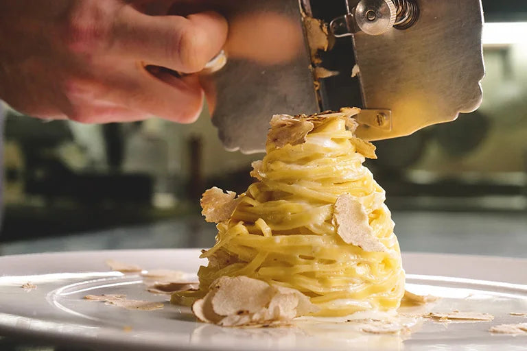 Pasta with truffles being finished table side as fresh truffle is shaved with a metal slicer, capturing an authentic fine dining moment