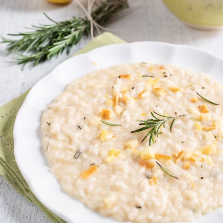 Lemon risotto spread in a wave on a wide white plate, finished with grated lemon zest and a drizzle of extra virgin olive oil