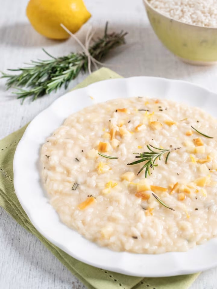 Lemon risotto spread in a wave on a wide white plate, finished with grated lemon zest and a drizzle of extra virgin olive oil