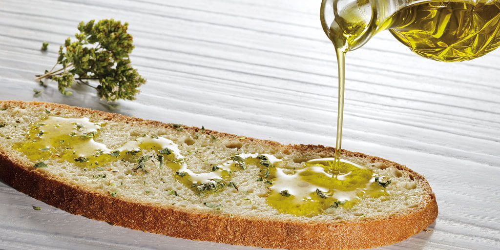Fresh extra virgin olive oil poured over bruschetta, showing the vibrant green color characteristic of early-harvest high-phenolic oil