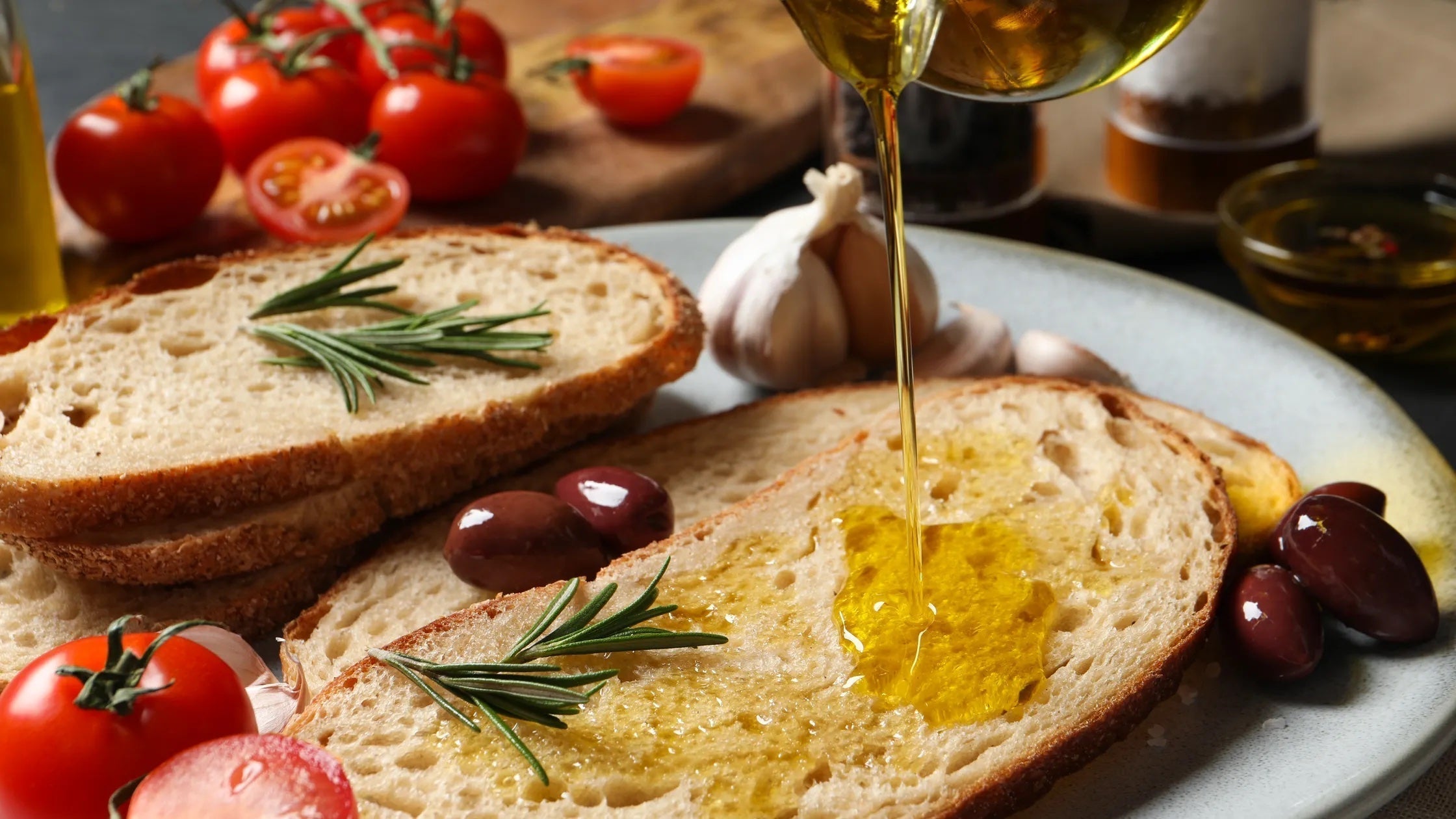 Extra virgin olive oil poured over bread with tomatoes, olives, garlic and rosemary