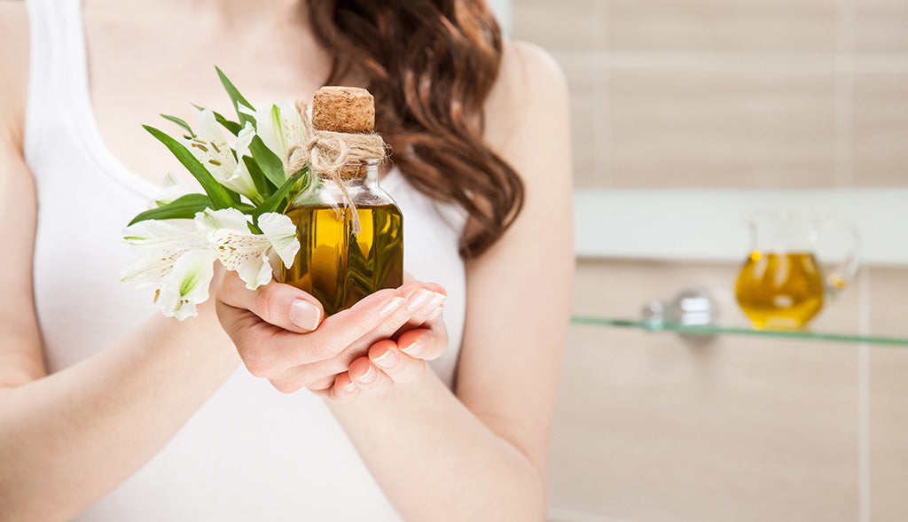 Woman holding a small glass bottle of olive oil for a skincare routine.