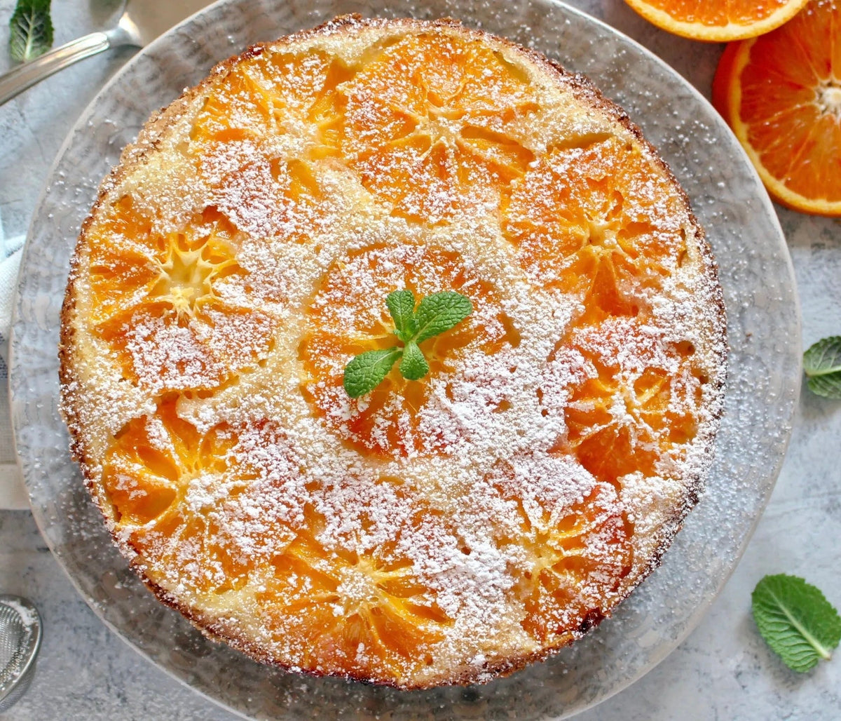 Upside-down orange olive oil cake topped with caramelized orange slices, powdered sugar and a sprig of mint, viewed from above