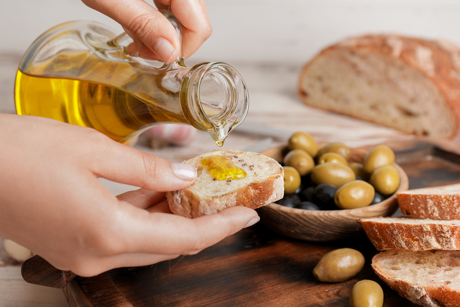 Extra virgin olive oil poured onto bread beside green and black olives