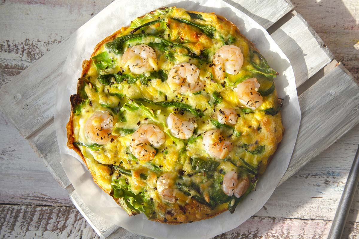 Shrimp and asparagus frittata finished with truffle oil, served warm on a rustic wooden table.
