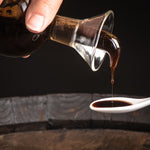 Balsamic vinegar of Modena poured slowly onto a white tasting spoon.
