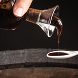 Balsamic vinegar of Modena poured slowly onto a white tasting spoon.