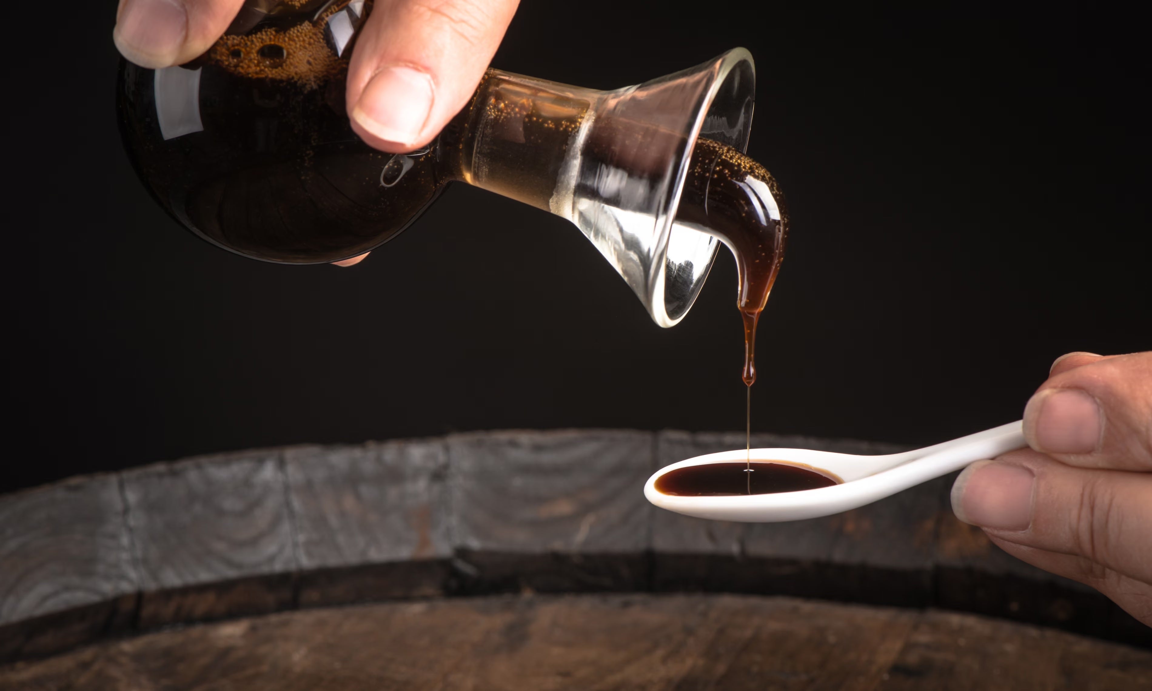 Balsamic vinegar of Modena poured slowly onto a white tasting spoon.