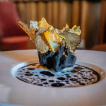 Plated black truffle dish with shaved truffle and crispy wafer on broth
