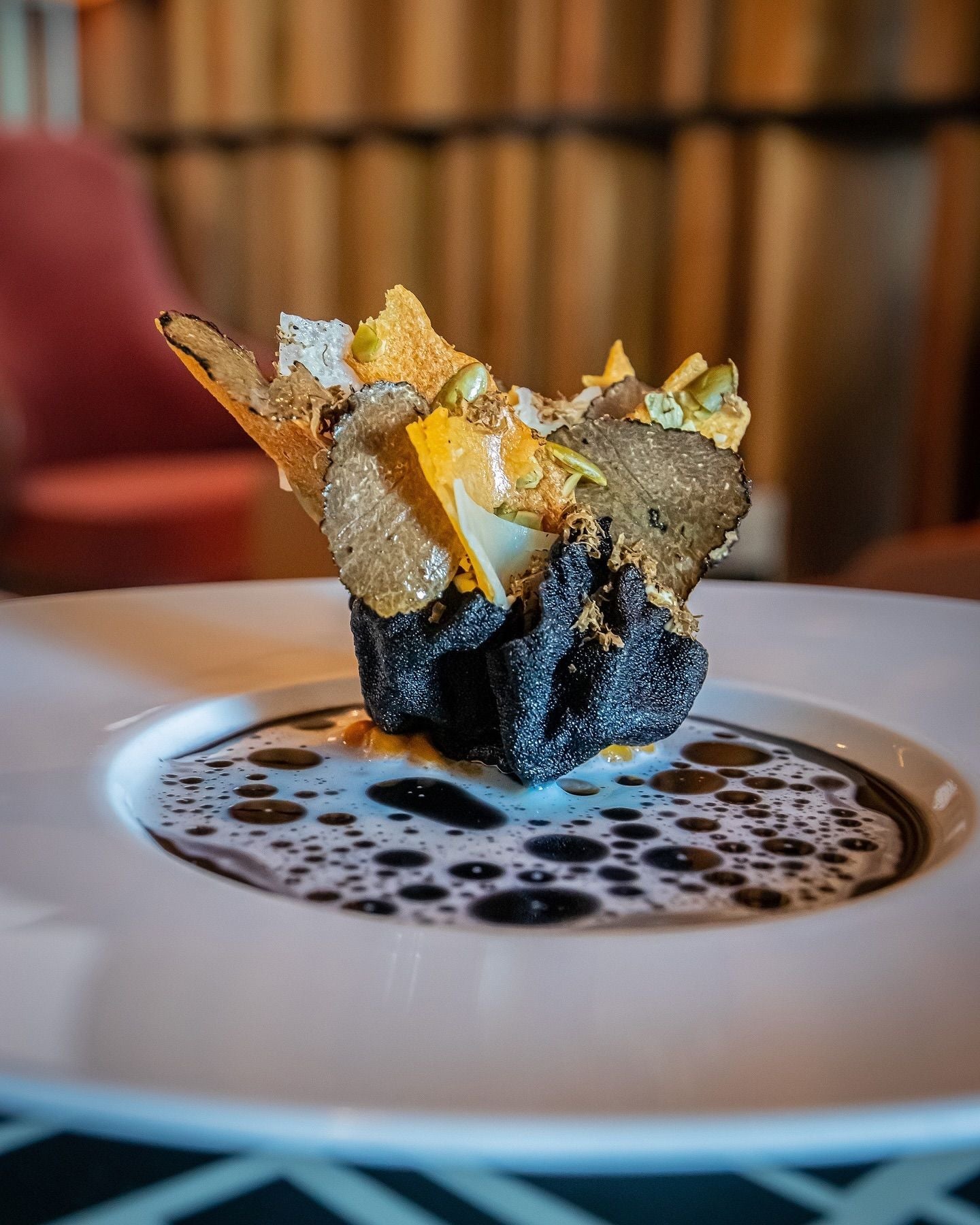 Plated black truffle dish with shaved truffle and crispy wafer on broth